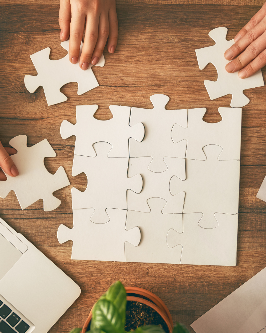 Mains assemblant un puzzle blanc sur table en bois, symbole de collaboration et de stratégie